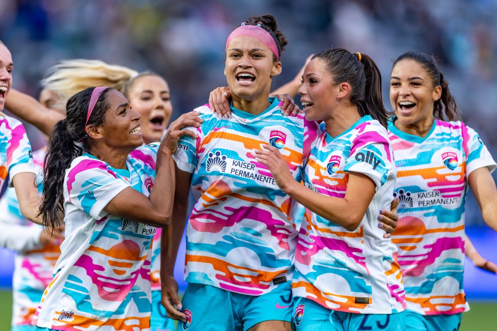 San Diego Wave players celebrating a goal with smiles and excitement during a soccer match.