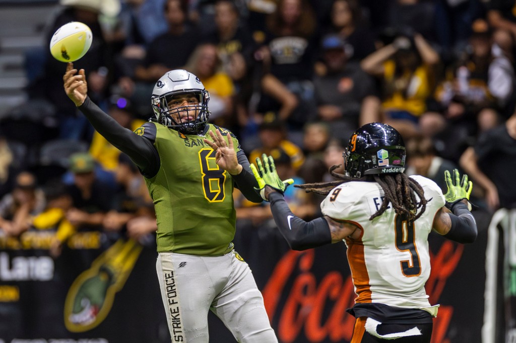 San Diego Strike Force quarterback throwing a pass while being pressured by an Arizona Rattlers defender during an indoor football game.