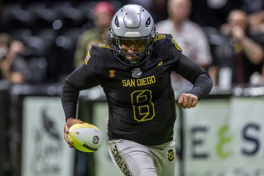 San Diego Strike Force player running with the football during a game, wearing a black jersey with yellow accents and a silver helmet.